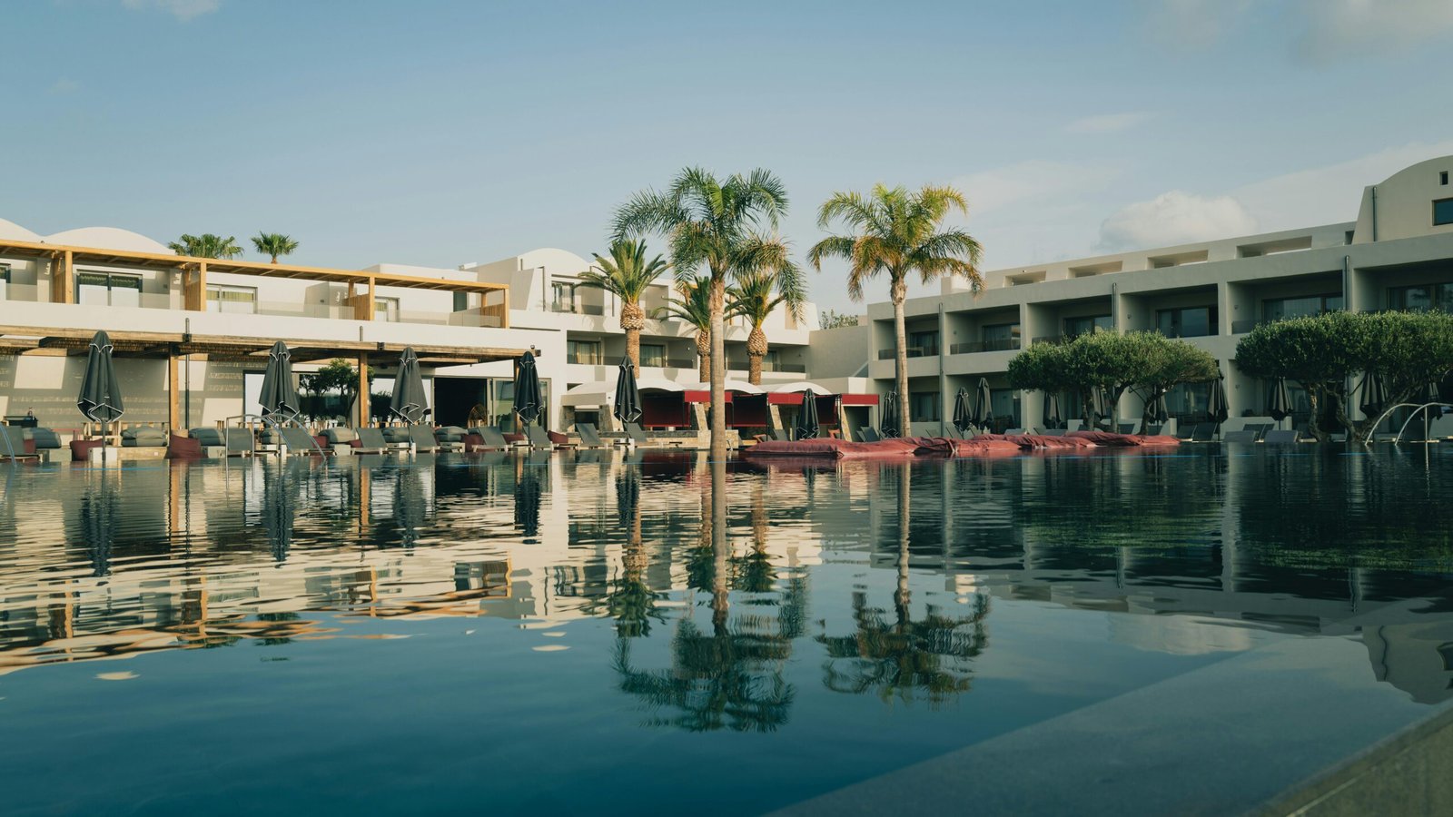 Elegant resort with a pool and palm trees under a clear blue sky in Greece.