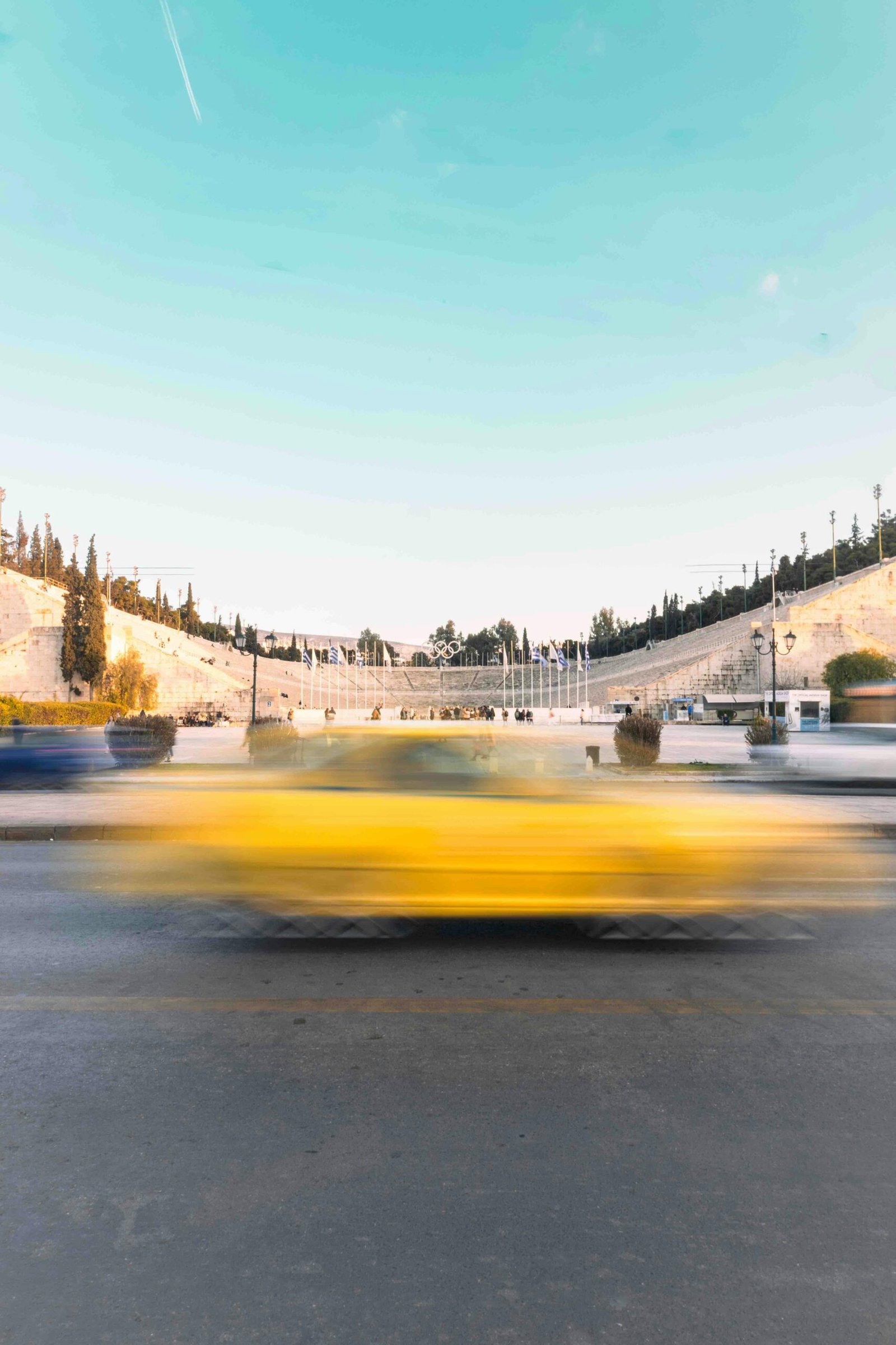 A vibrant motion blur of a yellow taxi passing by the historic Panathenaic Stadium in Athens, Greece.