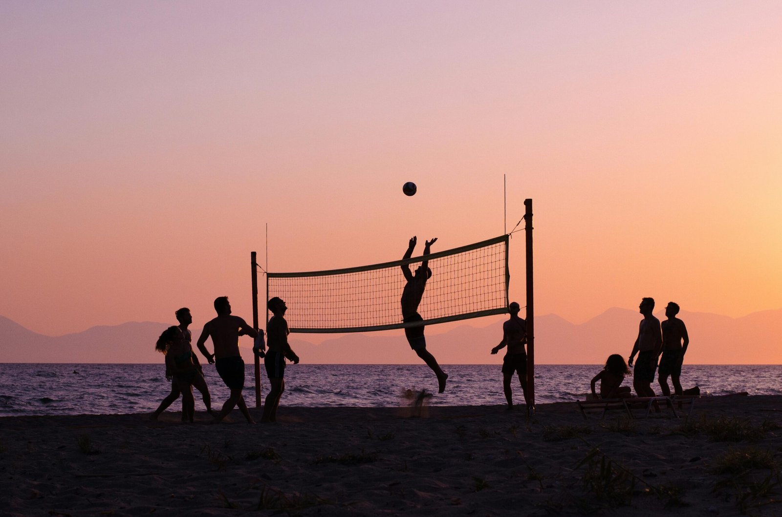 Silhouettes playing volleyball on a Greek beach during a stunning sunset.